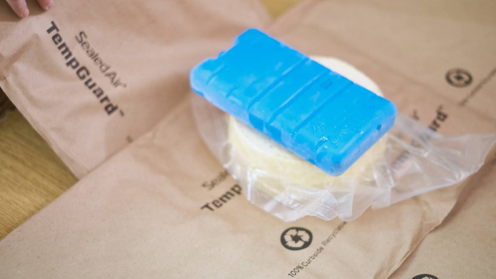 A round of fresh cheese with an ice pack on top, laid on an insulated liner before packing.